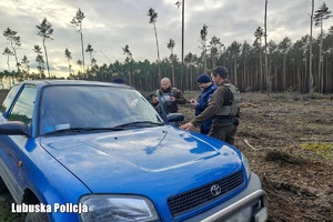 Policjant ze strażnikami leśnymi kontrolują pojazd.